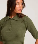 Blusa de punto texturizado color crema, con cuello polo, botones en el puño y mangas cortas.