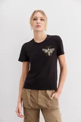 Remera negra de algodón con calce al cuerpo, mangas cortas y cuello redondo. Presenta un bordado frontal de abeja con canutillos dorados y plateados.