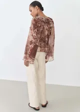 Blusa de gasa con estampado animal print en tonos marrones, cuello de pico con cierre de lazo, volantes en cuello y mangas largas acampanadas.