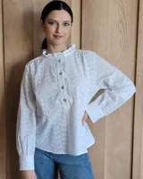 Camisa a rayas verticales color beige y blanco, de corte holgado, con cuello con volados, cierre parcial con botones y mangas largas con puños abotonados.