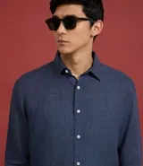 Camisa marrón claro de lino, de corte clásico, con cuello inglés, manga larga y cierre frontal con botones blancos.