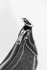 Cartera negra de denim con costuras blancas en contraste, cierre superior con cremallera y asa corta con hebilla ajustable.