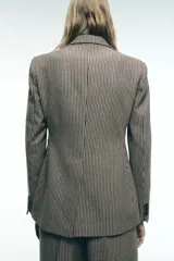 Blazer de cuello solapa y manga larga con estampado de cuadros en tonos marrón y blanco. Tiene bolsillos con solapa en el delantero, abertura en la espalda y cierre frontal con botones.
