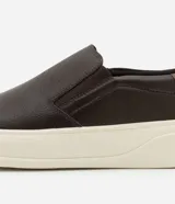 Championes slip on de cuero color marrón oscuro con detalle de cuero marrón claro en el talón y suela de goma color crema.