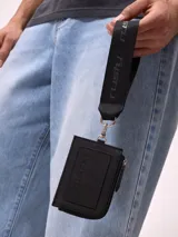 Billetera tarjetero negra de poliuretano con cierre y correa para colgar al cuello con logo Rusty estampado.