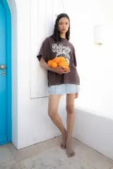 Remera marrón de corte amplio con estampado de texto y dibujo en color blanco.