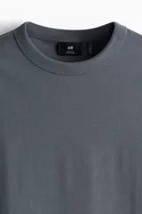 Remera gris de punto pesado con cuello redondo ribeteado, hombros caídos y bajo recto. Corte holgado confeccionada con tejido funcional COOLMAX®, una fibra exclusiva de poliéster de secado rápido que elimina la humedad y regula la temperatura corporal.