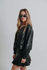 Campera bomber color beige de cuero, con cuello redondo, cierre frontal con botones a presión, mangas largas con puños elásticos y detalles de tachas metálicas en hombros y espalda.