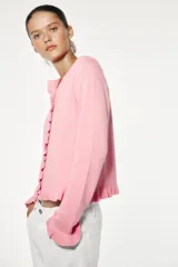 Chaqueta de punto rosa con cuello redondo y manga larga. Detalle de volantes en los bordes y cierre frontal con botones.