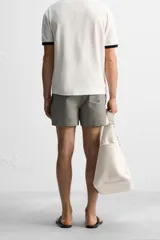 Short de baño con textura seersucker a rayas verticales azul marino y blanco. Tiene cintura elástica ajustable con cordón, bolsillos frontales y traseros, aberturas laterales en el bajo y forro interior.