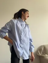 Camisa celeste a rayas verticales blancas, con cuello mao con volados y volados frontales.