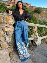 Pantalón de jeans azul con corte palazzo, cintura alta con lazo y bordado decorativo en el ruedo.