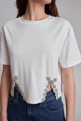 Remera blanca de algodón con cuello redondo y mangas cortas. Presenta apliques de strass en los laterales del ruedo.
