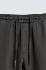 Pantalón jogger negro de corte slim fit, confeccionado en tejido de algodón con cintura elástica ajustable con cordón, bolsillos frontales y traseros de vivo, y bajo con puño elástico.