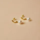 Par de aros colgantes de oro amarillo 18k con perlas de cultivo blancas. El aro es de tipo medio aro y la perla cuelga del mismo.