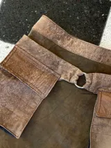 Falda corta de cuero gamuza color marrón oscuro, con diseño utilitario que incluye grandes bolsillos frontales con solapa y un anillo metálico en la cintura. Incluye un cinturón removible a juego.