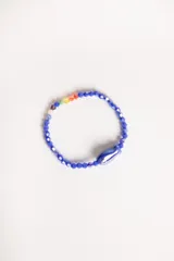 Pulsera elástica de cuentas facetadas azules con un dije de pez azul y detalles de cuentas de colores en un sector.