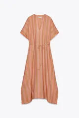 Vestido largo tipo kaftán confeccionado en lino a rayas verticales en tonos naranja y verde. Tiene cuello redondo con escote en V, mangas cortas amplias, acabado deshilachado y cinturón de cordón en el mismo tejido.