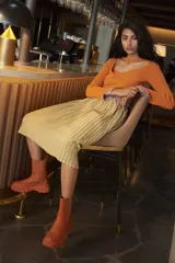 Buzo tejido color naranja con cuello halter desmontable con detalle de volados color lila en los bordes.