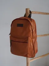 Mochila de cuero color marrón con forro de lino y cierres de bronce. Tiene un compartimento interno acolchado para computadora portátil.