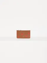 Tarjetero marrón de cuero vacuno liso con estampado de corazones rojos. Cuenta con bolsillo con cierre metálico, espacio para tarjetas y aplique metálico JCH en el frente.