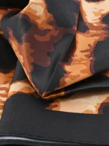 Pañuelo rectangular con estampado abstracto en tonos terracota, negro, blanco y beige.