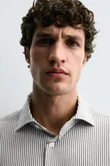 Camisa de manga larga con cuello italiano y cierre frontal de botonadura. Presenta un patrón de rayas verticales finas en tonos blanco y verde claro.