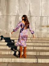 Vestido midi con estampado floral en tonos lila, amarillo y verde. Tiene escote fruncido con lazo ajustable, mangas largas abullonadas y tajo lateral.