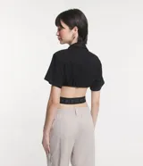 Camisa corta negra con cuello camisero, mangas cortas y aberturas laterales con elástico con letras blancas.