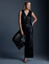 Enterito de lentejuelas marca Ninety, color negro, con escote en V cruzado y diseño sin mangas. Presenta cintura elastizada con lazo de ajuste, bolsillos frontales y abertura en la espalda con cierre invisible. Incluye forro interno a tono.