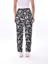 Pantalón babucha de tela estampada con hojas en tonos rosa, naranja y azul, con cintura elastizada y lazo para ajustar.