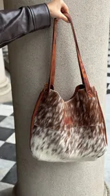 Bolso tipo tote de cuero con pelo de vaca color marrón y blanco. Tiene doble asa de cuero marrón y bolsillo interno.