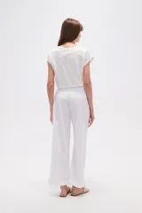 Pantalón blanco de algodón con calce recto y tiro bajo. La tela presenta bordados tipo calado (broderie) a lo largo de toda la prenda.