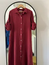 Camisola larga de lino color bordó, con cuello camisero, cierre frontal de botones y mangas largas con presilla para enrollar.