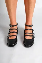 Chatas de cuero negro con punta fina, cuatro tiras horizontales con hebilla y pulsera al tobillo.