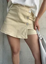 Short pollera color beige con botones plateados en el frente.