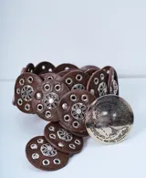 Cinturón marrón de cuero con apliques metálicos plateados en forma de círculos con diseños florales y ojales.