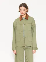 Chaqueta verde militar de algodón con cuello marrón de pana, cierre frontal con botones dorados, bolsillos plaqué en la parte superior e inferior y corte holgado.