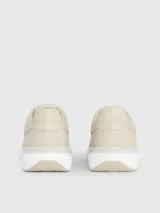 Zapatillas urbanas color beige, confeccionadas en cuero y tela, con suela blanca y cordones. Presentan monograma de la marca en el lateral.