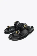 Sandalias planas negras con dos tiras anchas y hebillas doradas.
