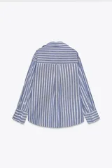 Camisa de algodón a rayas verticales azules y blancas con hilo metalizado, cuello solapa y escote pico. Manga larga acabada en puño, bajo asimétrico y cierre frontal con botones.