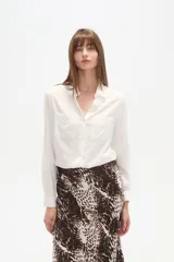 Camisa de viscosa color crema con finas rayas verticales negras, corte al cuerpo, cuello camisa y dos bolsillos frontales con tapa. Posee botones frontales y mangas largas con puño.