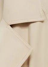 Abrigo largo color beige con cuello de solapa, trabillas en los hombros y cinturón tipo batín.
