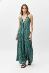 Mono largo de poliéster con estampado geométrico en tonos verde y beige. Tiene breteles finos que se atan en la nuca, escote halter y corte ancho.