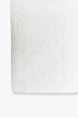 Camiseta blanca de algodón con cuello redondo y manga corta. Presenta bordados florales a tono en el lateral derecho del pecho y en la parte inferior izquierda.