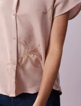 Camisa color beige con estampado de hojas marrones, de manga corta, con cuello a la base con solapa y escote en V.