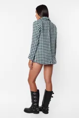 Conjunto de blazer y short de tiro alto con estampado pata de gallo en tonos verde y blanco. El blazer es de corte oversize, con solapas y cierre cruzado con botones. El short es de corte ajustado con terminaciones al corte con costura de seguridad. Se completa el look con un top blanco y botas de cuero negras.