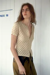 Top color crema de tejido de punto calado con patrón de rombos, cuello redondo, manga corta y cierre frontal con ganchos metálicos.