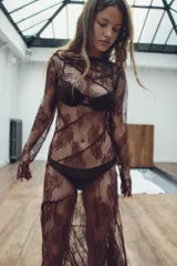 Vestido midi semitransparente de encaje floral color borgoña, con cuello barco, mangas largas y espalda con escote en V. Presenta costuras marcadas y terminaciones onduladas.