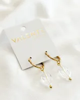Aros colgantes dorados con forma de argolla, con dije de cristal transparente facetado y bolita dorada en el extremo inferior.